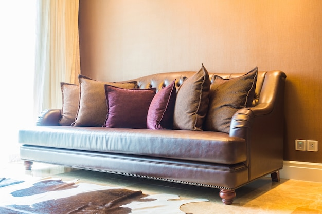 Коричневый кожаный диван с несколькими подушками в хорошо освещенной гостиной.